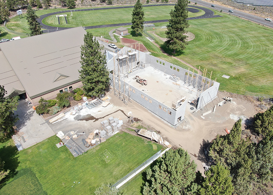 A drone-captured image of the walls and foundation of the auxillary gym. Athletic fields can be seen in the background